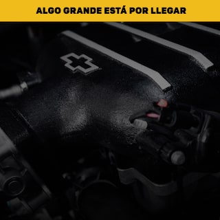 Primer plano de una cubierta de motor Chevrolet negra con el logotipo de corbatín debajo de un cartel amarillo con el texto Algo grande llegará.